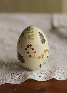 an egg with leaves painted on it sitting on a lace doily next to a wooden table