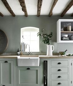 a kitchen with green painted cabinets and white counter tops, an open window above the sink