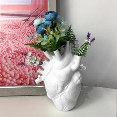 a white vase with flowers in it sitting on a table next to a framed painting