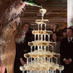 a group of people standing around a tall cake with wine glasses on top of it