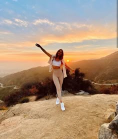 a woman standing on top of a mountain with her arms in the air and one hand out