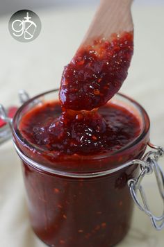 a wooden spoon full of jam on top of a glass jar filled with red liquid