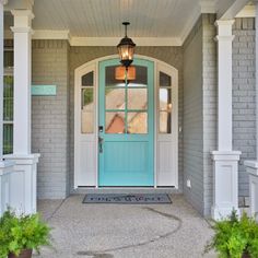 a blue front door with two potted plants on either side and one light hanging over the doorway