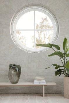 a round window in a white room with a wooden bench and potted plant next to it