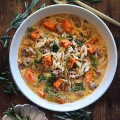 a white bowl filled with pasta, meat and vegetables on top of a wooden table