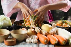 a woman in pink shirt preparing food on top of a wooden table next to bowls