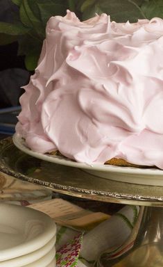 a cake with pink frosting sitting on top of a table next to plates and flowers