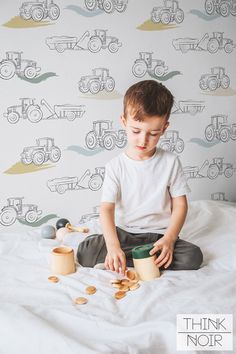 a young boy sitting on top of a bed holding a cup and playing with wooden toys