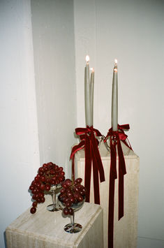 two candles with red bows and cherries on a table