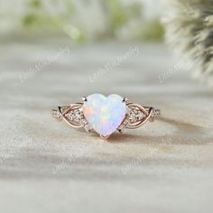 an opal heart shaped ring with diamonds in the middle on top of a table