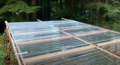 the roof of a greenhouse is covered with plastic sheeting and wood planks as it sits in front of some trees