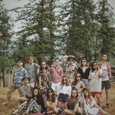 a group of people standing and sitting on top of a grass covered field next to trees