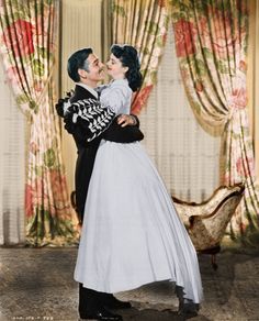 a man and woman kissing in front of curtains