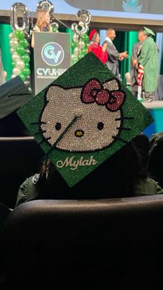 a hello kitty graduation cap sitting on the back of a chair in front of people