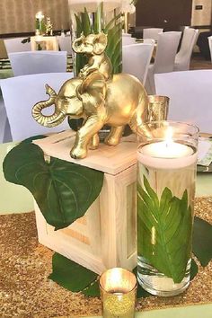 a table topped with candles and vases filled with green plants next to an elephant figurine