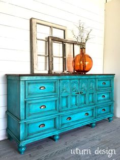 a blue dresser with two vases on top and a mirror above it in front of a white wall