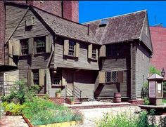 an old wooden house with many windows and lots of greenery in front of it