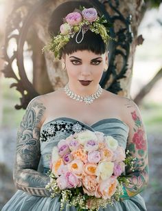 a tattooed woman in a blue dress holding a bouquet of flowers and wearing a tiara