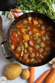 a pot filled with stew next to carrots, potatoes and celery on a table