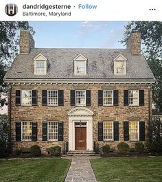 an old brick house with black shutters on the front and side windows, along with green grass