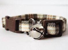 a brown and white plaid dog collar with a bell on it's side,