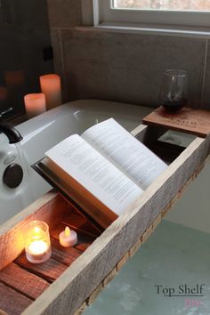 an open book sitting on top of a bath tub next to candles and a candle holder