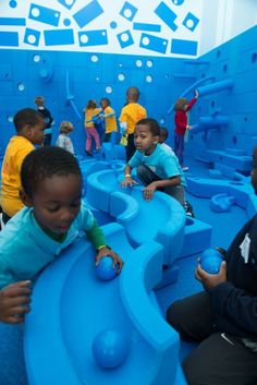 children playing in an indoor play area with blue walls and flooring, while adults look on