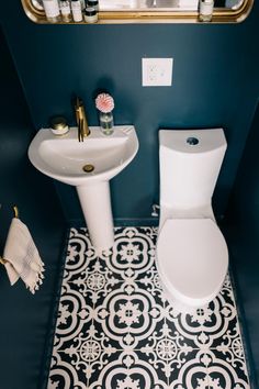 a white toilet sitting next to a sink in a bathroom under a mirror with gold trim