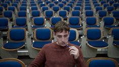 a man is sitting in a room full of blue chairs and brushing his teeth with an electric toothbrush