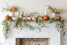 a mantel with candles, pumpkins and greenery in front of a brick fireplace