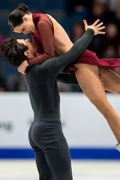 two people on ice skating in front of an audience and one is holding the other