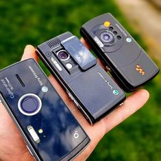 three cell phones sitting in the palm of someone's hand, one with a camera attached to it