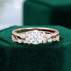 a diamond ring on top of a green velvet cushioned surface with the center stone surrounded by smaller round diamonds