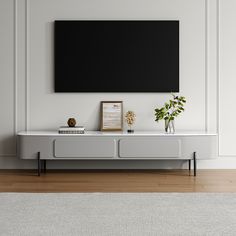 a white entertainment center with a black screen mounted on the wall above it and two vases filled with flowers