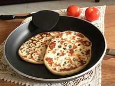 two pizzas in a pan on a table with tomatoes and an iron skillet