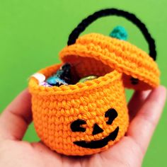 a crocheted pumpkin basket with candy in it is held by someone's hand