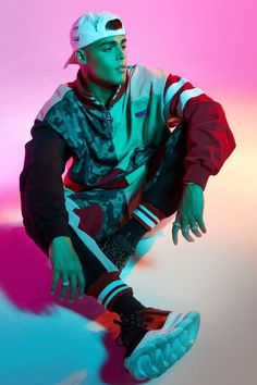 a man sitting on top of a skateboard in front of a pink and blue background