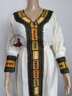 This stunning Habesha Kemis is crafted from 100% cotton Axum Shukor Menen fabric and adorned with 100% handmade Tibeb, reflecting the skill of Ethiopian artisans. Designed as one-size-fits-all, this dress offers comfort and style for any occasion. For custom sizing, send us your measurements, and we'll be delighted to create a personalized fit. Perfect for cultural celebrations, weddings, and more, this timeless piece is a celebration of Ethiopian heritage! Traditional Fitted Cotton Kaftan, Fitted Cotton Traditional Kaftan, Folk Cotton Dresses For Festivals, Traditional Cotton Festival Dresses, Cotton Dresses With Traditional Patterns For Festival, Cotton Dresses With Traditional Embroidered Patterns, Cotton Dresses With Multicolor Embroidery And Traditional Patterns, Traditional Multicolor Cotton Dress, Folk Style Cotton Dress With Traditional Patterns