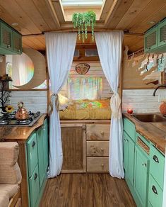 an interior view of a small camper with wood floors and green cabinets, white drapes on the windows