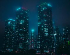 two tall buildings lit up at night in the city with fog and smoggy skies