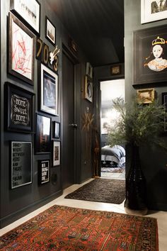 a hallway with black walls and framed pictures on the wall, rugs and potted plant