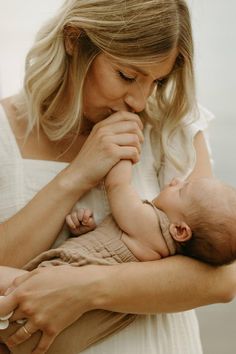 a woman holding a baby in her arms and touching it's face with both hands