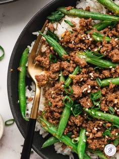 a bowl filled with meat and green beans on top of white rice next to a spoon