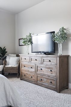 a bedroom with a bed, dresser and television on the wall in front of it