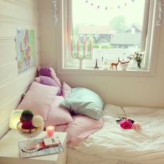 a bed with pink and blue pillows next to a window in a room filled with toys