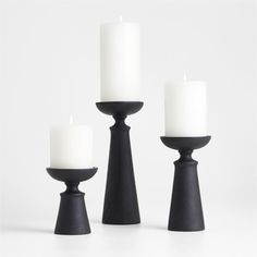 three black candle holders with white candles in them