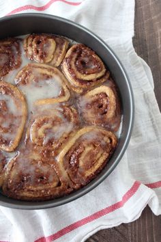 cinnamon buns in a pan on a table next to a cup of coffee and napkin