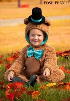 a little boy dressed up as a teddy bear sitting in the grass wearing a top hat and bow tie