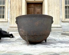 a large metal pot sitting on top of a stone floor next to a building with columns