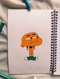 a notebook with a drawing of a cartoon character on the front and back cover, surrounded by colored pencils